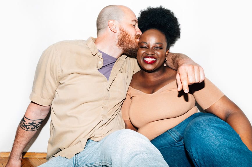 Portrait of white man kissing black woman in front of white background
